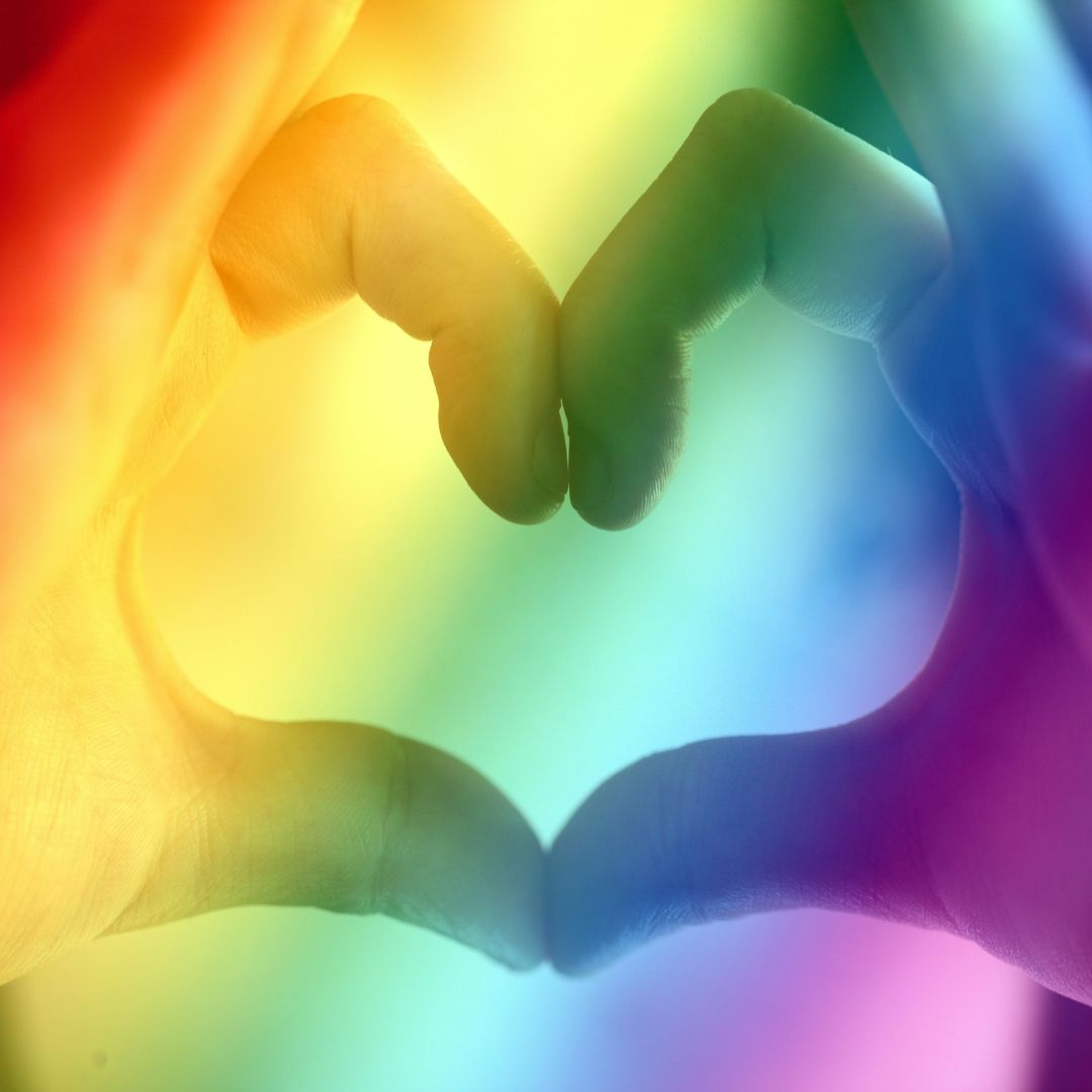 two hands making a heart shape with a rainbow coloured background